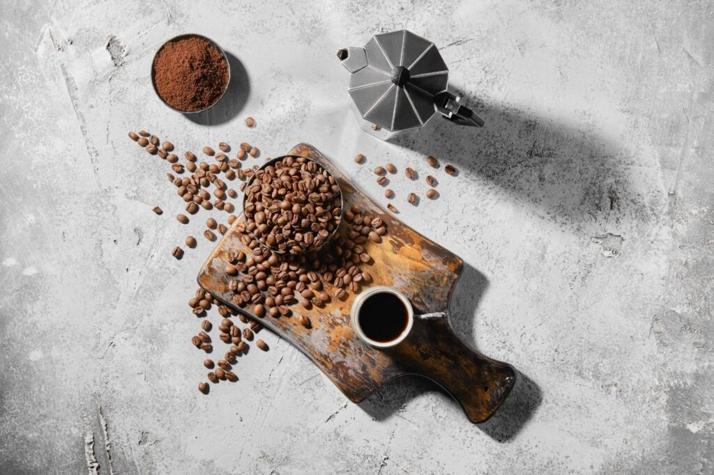 Espresso Beans sit in a bowl on a wooden serving board near a cup of grounds.