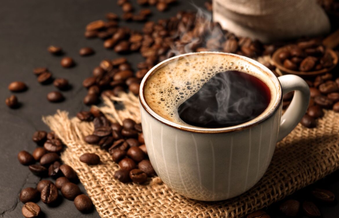 Steaming black coffee in a cup surrounded by roasted beans on burlap fabric