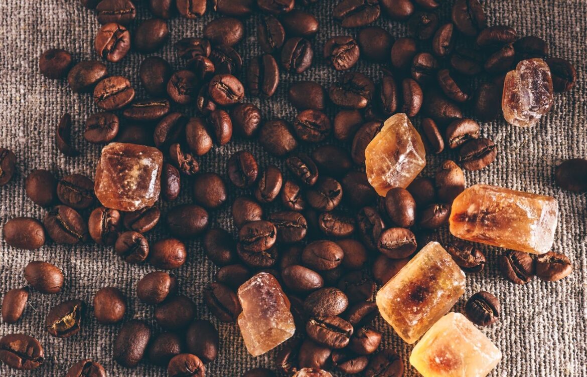 Roasted coffee beans next to crystalline sugar granules on a tabletop